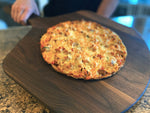 Whole pizza served on a walnut pizza peel in a kitchen.