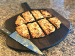 Sliced pizza on a walnut pizza peel with a pizza cutter alongside.