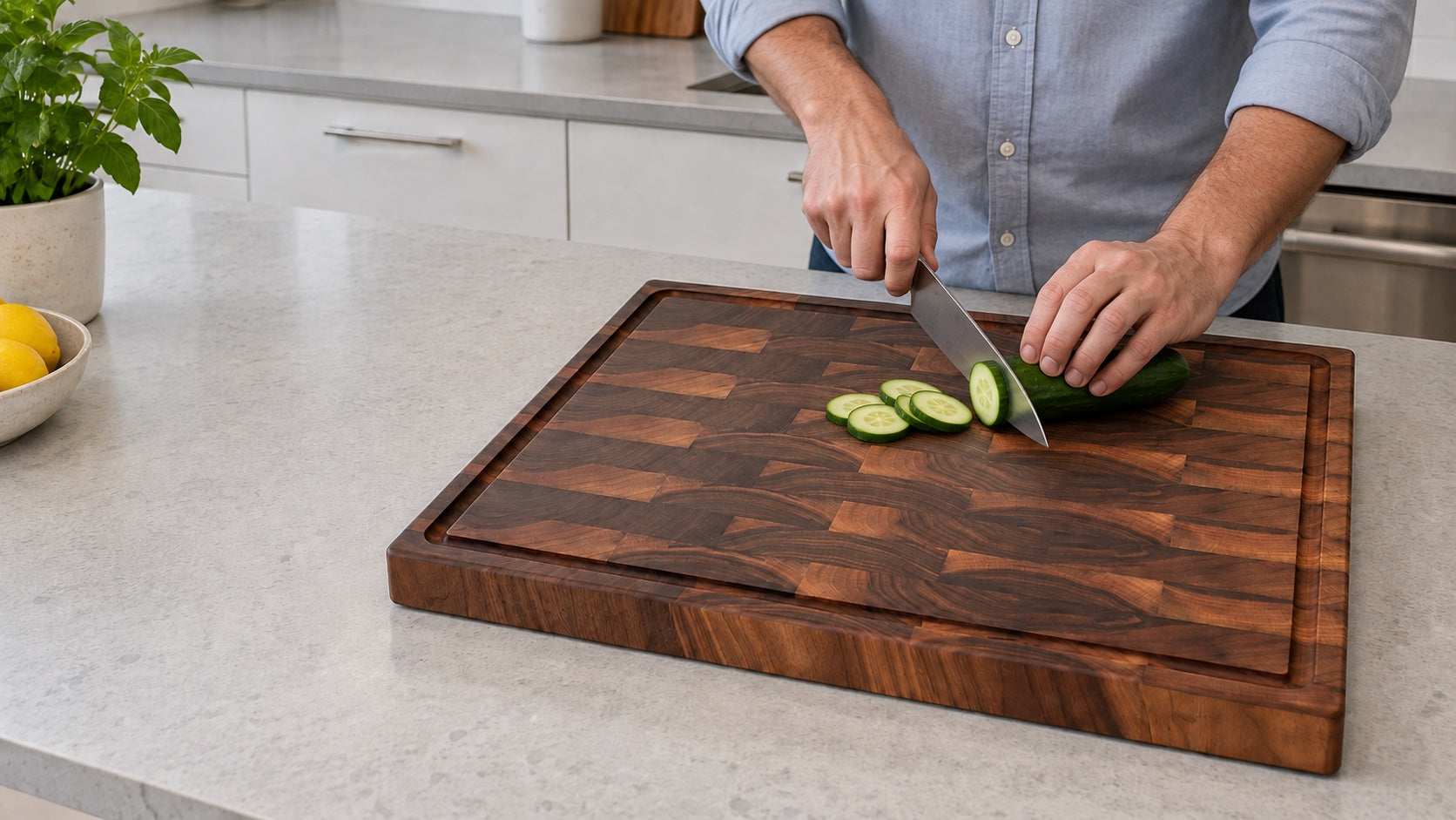 Close-up of hands slicing a cucumber on a Refine W24EG walnut end-grain cutting board in a modern kitchen with neutral daylight.